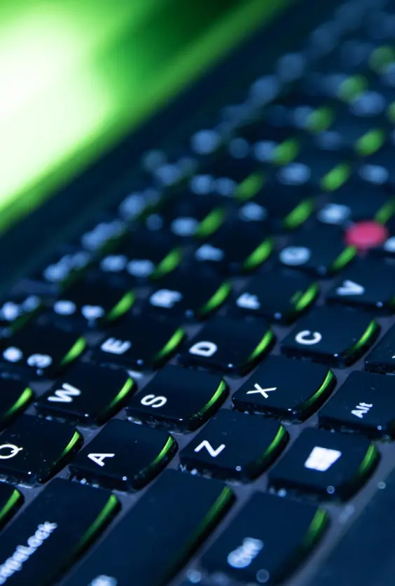 Close-up of backlit gaming laptop keyboard with green accents and red TrackPoint